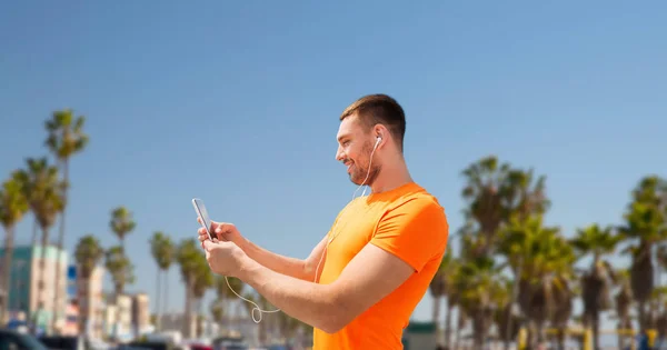 Smiling young man with smartphone and earphones — Stock Photo, Image