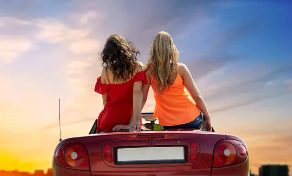 Mujeres sentadas en un coche descapotable sobre la puesta de sol de la ciudad —  Fotos de Stock