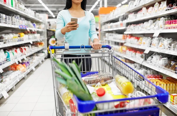 Vrouw met smartphone kopen van eten in supermarkt — Stockfoto