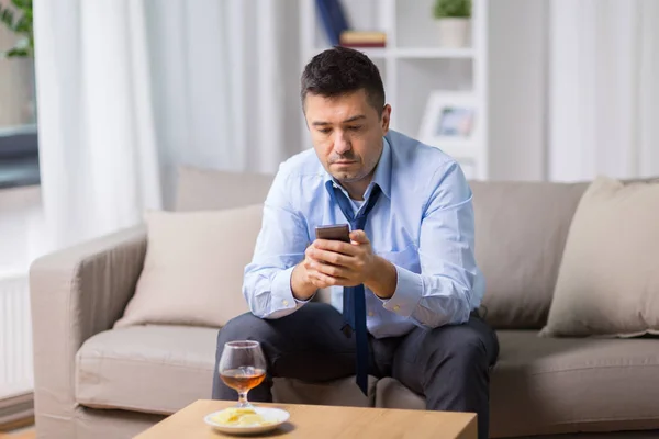 Pijany mężczyzna ze smartfonem i alkohol w domu — Zdjęcie stockowe