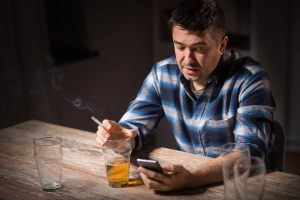 Мужчина с сотовым телефоном пьет алкоголь и курит — стоковое фото