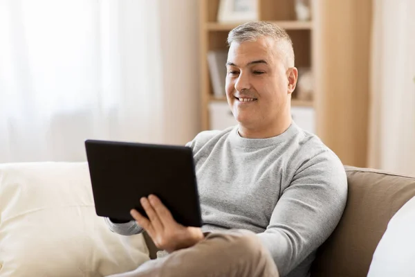 Uomo con tablet pc seduto sul divano di casa — Foto Stock