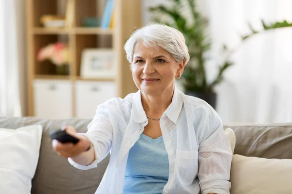 Mulher idosa com controle remoto assistindo tv em casa — Fotografia de Stock