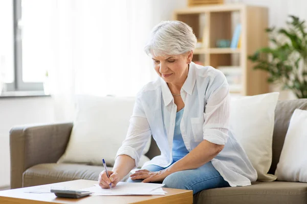 Mujer mayor con papeles y calculadora en casa — Foto de Stock