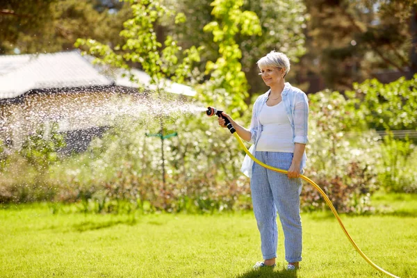 senior woman watering lawn by hose at garden