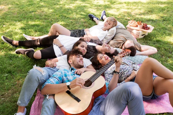 friends with guitar chilling on picnic blanket