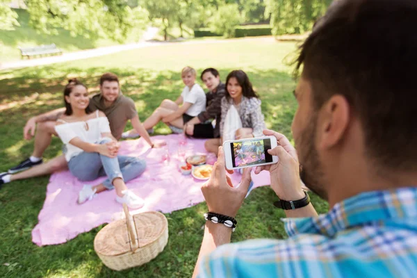 Uomo fotografare gli amici da smartphone al picnic — Foto Stock