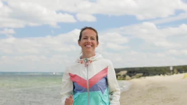 Улыбающаяся женщина бежит вдоль пляжа — стоковое видео
