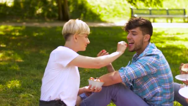 Счастливые друзья едят клубнику на летнем пикнике — стоковое видео