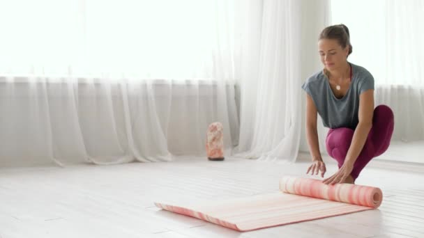 Женщина скручивает коврик в студии йоги или спортзале — стоковое видео
