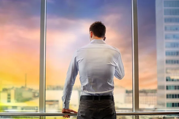 Hombre de negocios llamando en el teléfono inteligente en la ventana de la oficina —  Fotos de Stock