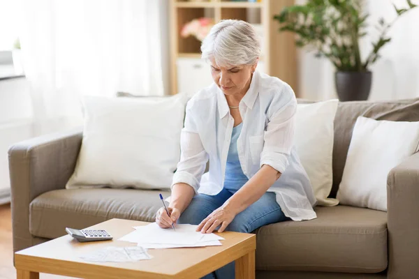 Senior vrouw met papieren en rekenmachine thuis — Stockfoto