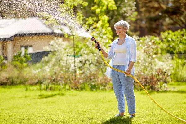 Senior femme arrosage pelouse par tuyau au jardin — Photo