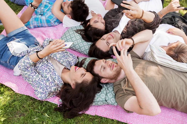 Amigos con teléfonos inteligentes en manta de picnic — Foto de Stock