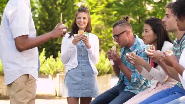 Amigos comendo sanduíches e falando no parque — Vídeo de Stock