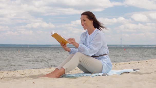 Lykkelig smilende kvinde læser bog om sommeren strand – Stock-video