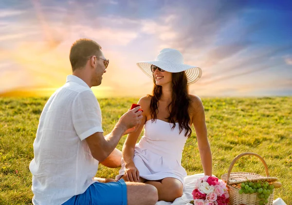 Pareja sonriente con una pequeña caja de regalo roja en el picnic —  Fotos de Stock