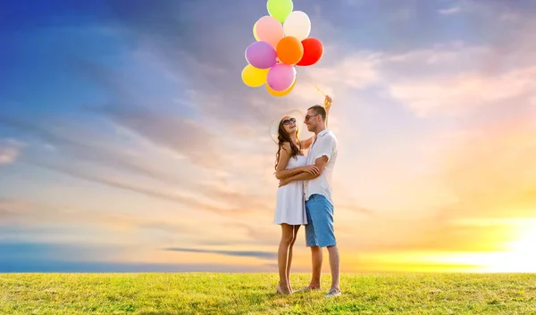 Happy couple with balloons over sunset sky — Stock Photo, Image