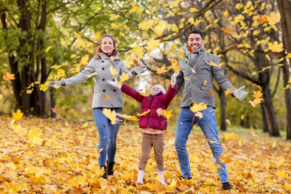 Família feliz brincando com folhas de outono no parque — Fotografia de Stock