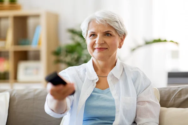 Senior woman with remote watching tv at home — Stock Photo, Image