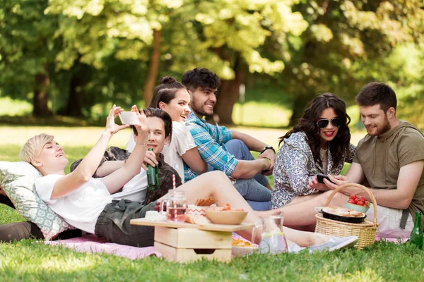 Amigos con teléfonos inteligentes en el picnic en el parque de verano — Foto de Stock