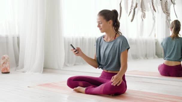 Женщина со смартфоном в студии йоги — стоковое видео