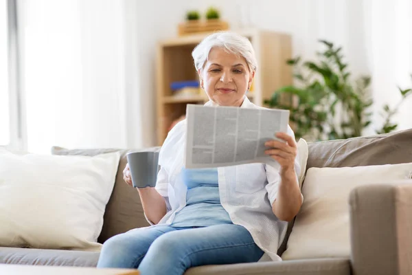 Mulher sênior com café lendo jornal em casa — Fotografia de Stock