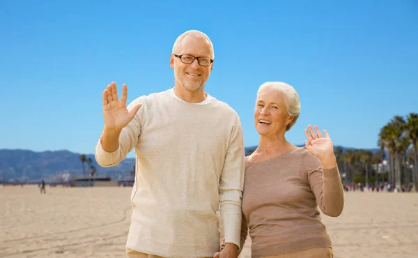 Happy senior couple waving hands over venice beach — Stock Photo, Image