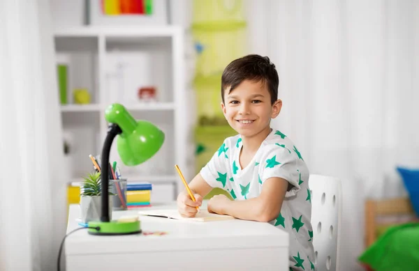 Glücklicher kleiner Junge schreibt zu Hause an Notizbuch — Stockfoto