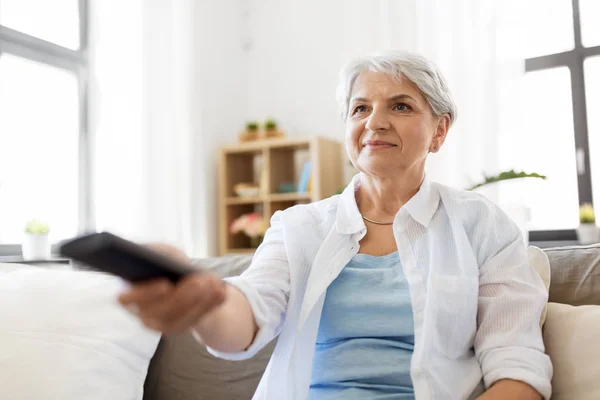 Senior vrouw met externe tv kijken thuis — Stockfoto