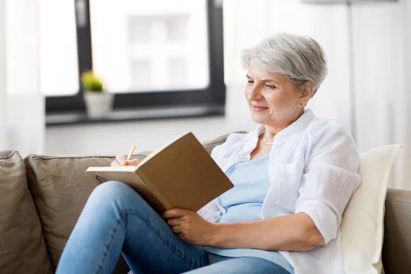 Wanita senior menulis ke notebook atau buku harian di rumah — Stok Foto