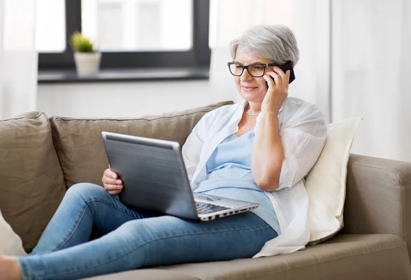 Donna anziana con laptop che chiama su smartphone — Foto Stock