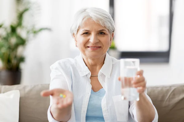 Senior woman with water and medicine at home — Stock Photo, Image