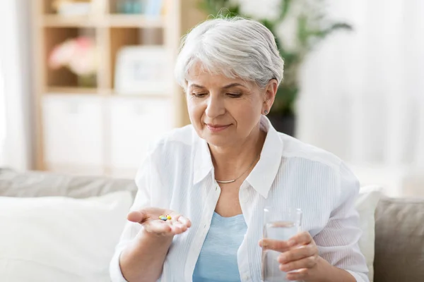 Donna anziana con acqua che prende la medicina a casa — Foto Stock