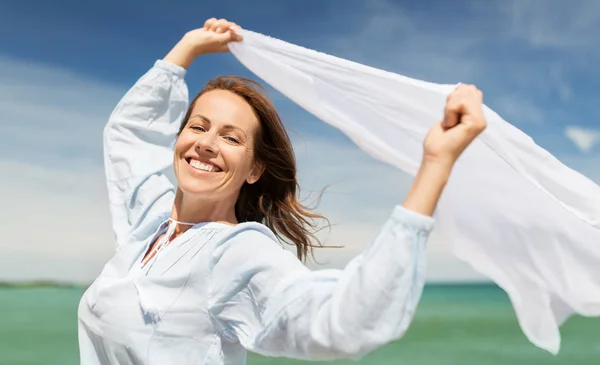 Gelukkige vrouw met sjaal wuiven in de wind op strand — Stockfoto