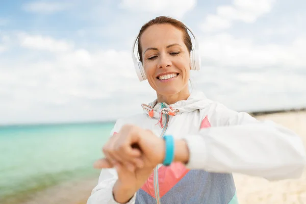 Kvinna med hörlurar och fitness tracker på stranden — Stockfoto