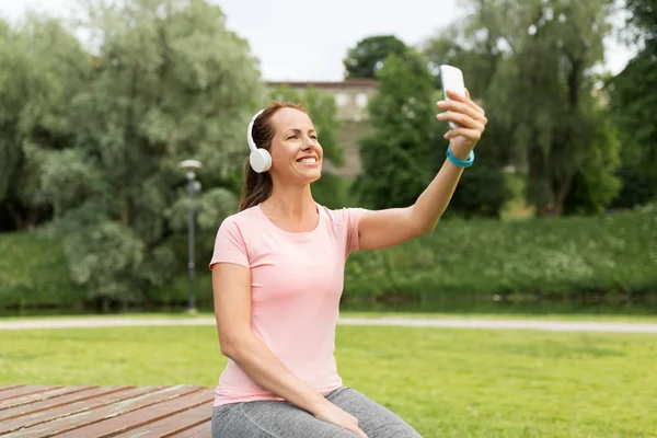 Nainen puhelimissa vie selfie älypuhelimella puistossa — kuvapankkivalokuva