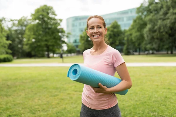 Femme souriante heureuse avec tapis d'exercice au parc — Photo