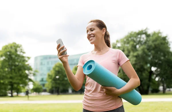 Mulher com tapete de exercício e smartphone no parque — Fotografia de Stock