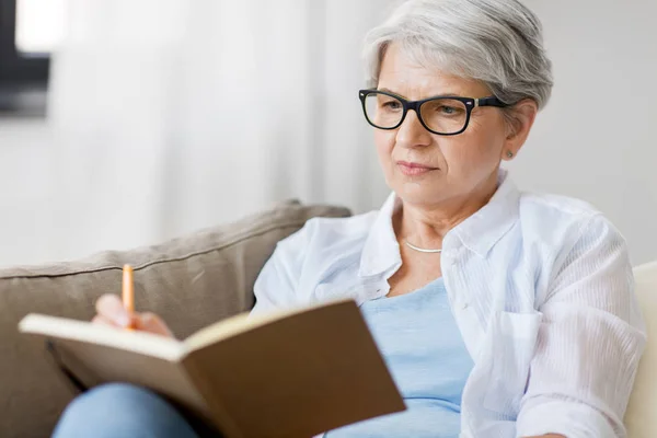 Wanita senior menulis ke notebook atau buku harian di rumah — Stok Foto