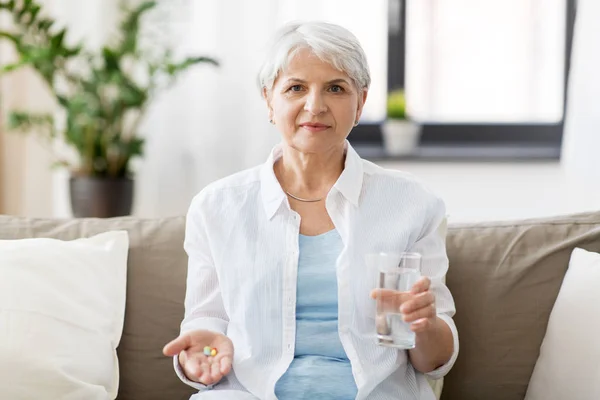 Donna anziana con acqua e medicina a casa — Foto Stock