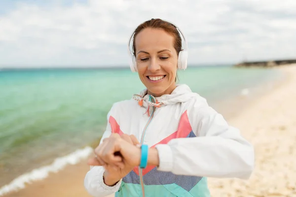 Kvinna med hörlurar och fitness tracker på stranden — Stockfoto