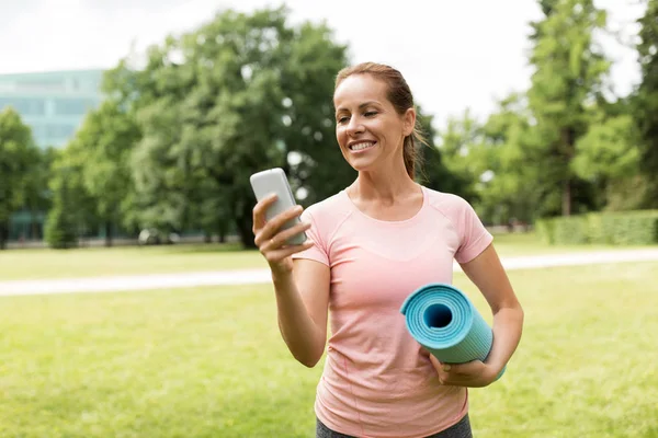 Kobieta z Mata do ćwiczeń i smartfon w parku — Zdjęcie stockowe