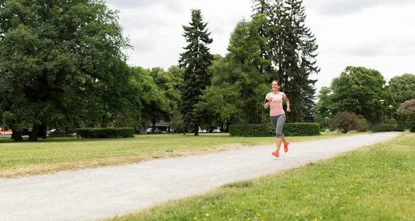 Frau mit Kopfhörern läuft in Park — Stockfoto
