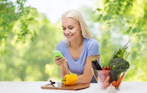 Mulher sorridente com smartphone cozinhar legumes — Fotografia de Stock