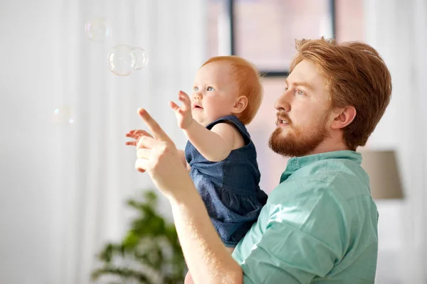 Pai e bebê filha com bolhas de sabão em casa — Fotografia de Stock