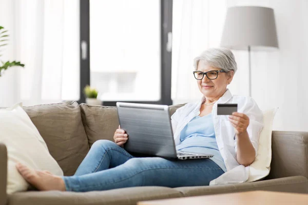 Evde dizüstü bilgisayarı ve kredi kartı olan yaşlı bir kadın var. — Stok fotoğraf