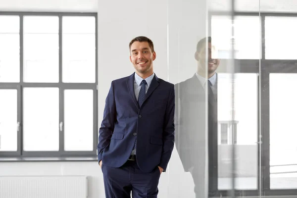 Uomo d'affari sorridente alla parete di vetro dell'ufficio — Foto Stock