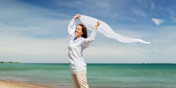 Lycklig kvinna med sjal som vajade i vinden på stranden — Stockfoto