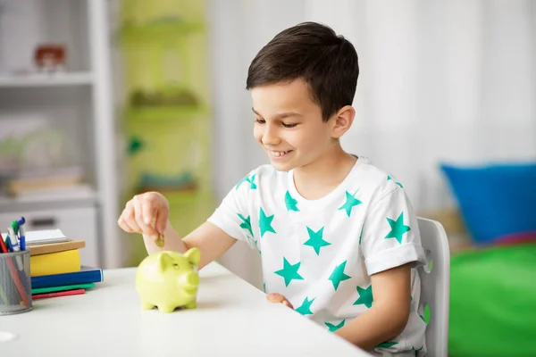 Little boy putting coin into piggy bank at home Royalty Free Stock Images
